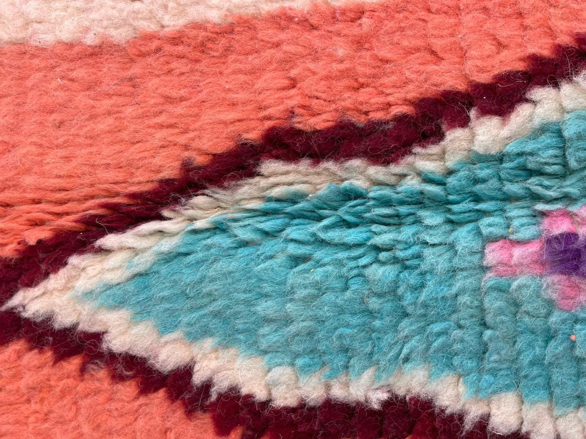 Detail close-up of a vintage Moroccan rug highlighting textured patterns in orange, turquoise, and pink.