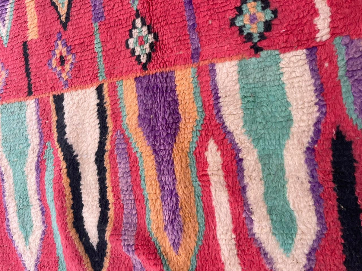 Detail close-up of a vintage Moroccan rug with colorful motifs and wool texture in red, purple, and turquoise.