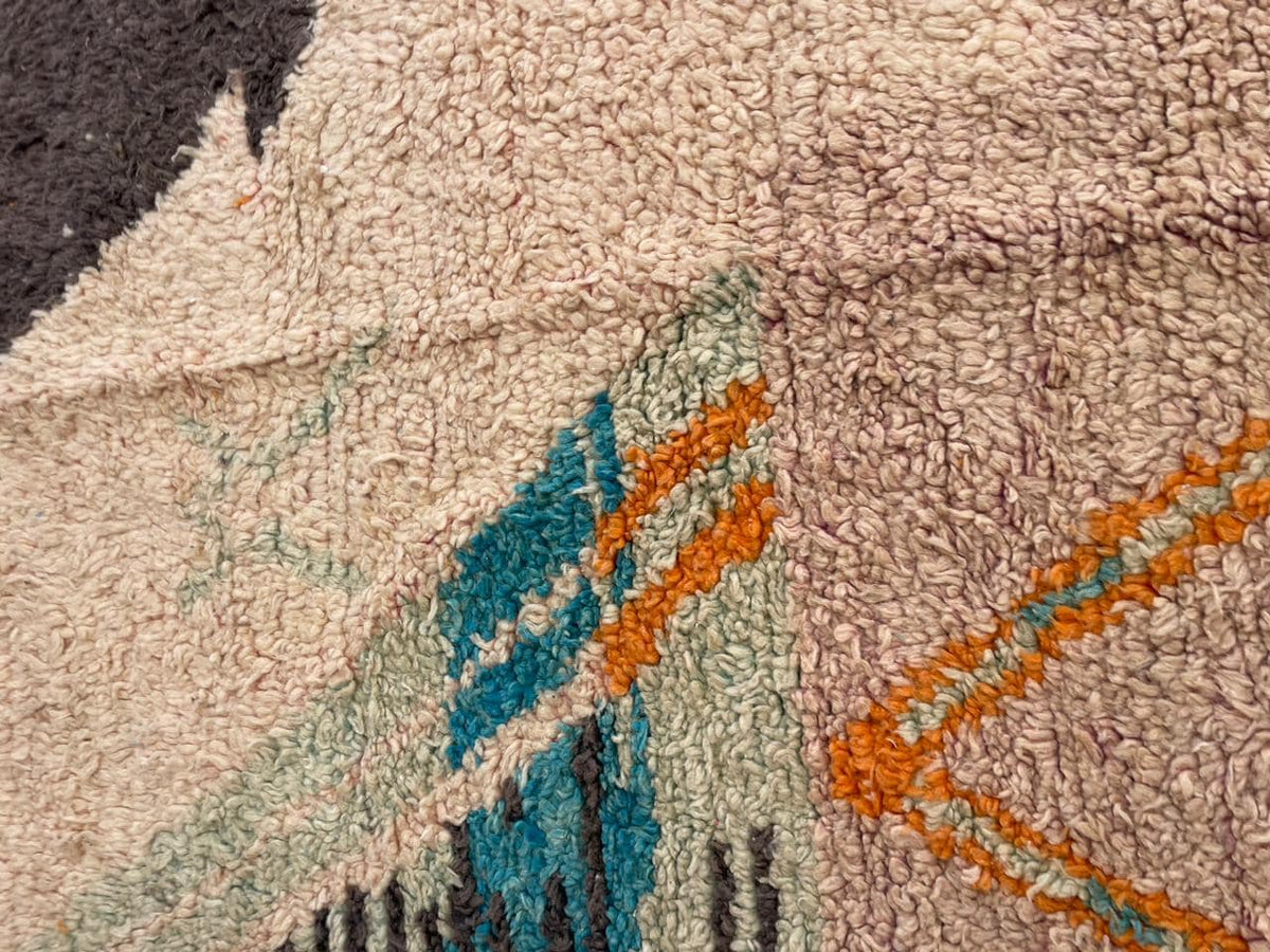 Detail view of a vintage Moroccan rug highlighting geometric patterns in beige, blue, and orange.