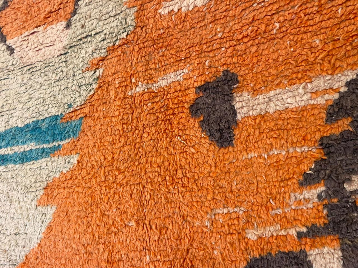 Detail view of a vintage Moroccan rug featuring a geometric design in orange, black, and cream.