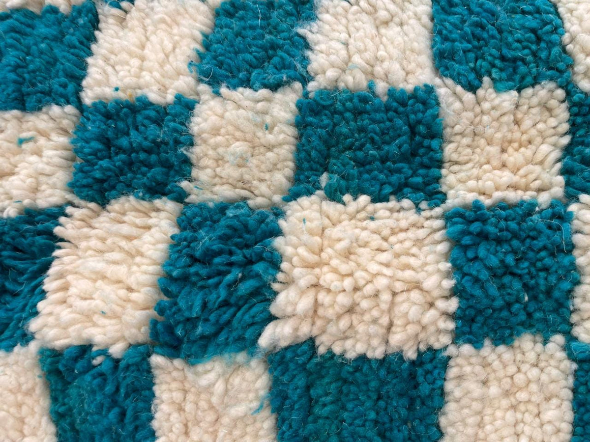 Close-up detail of the textured surface of a turquoise checkered rug.