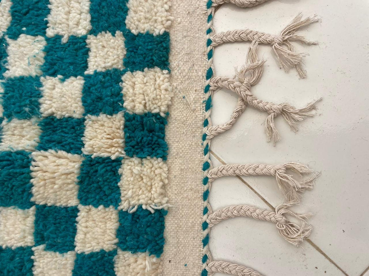 Detail view of the fringe edge on a checkered turquoise rug.