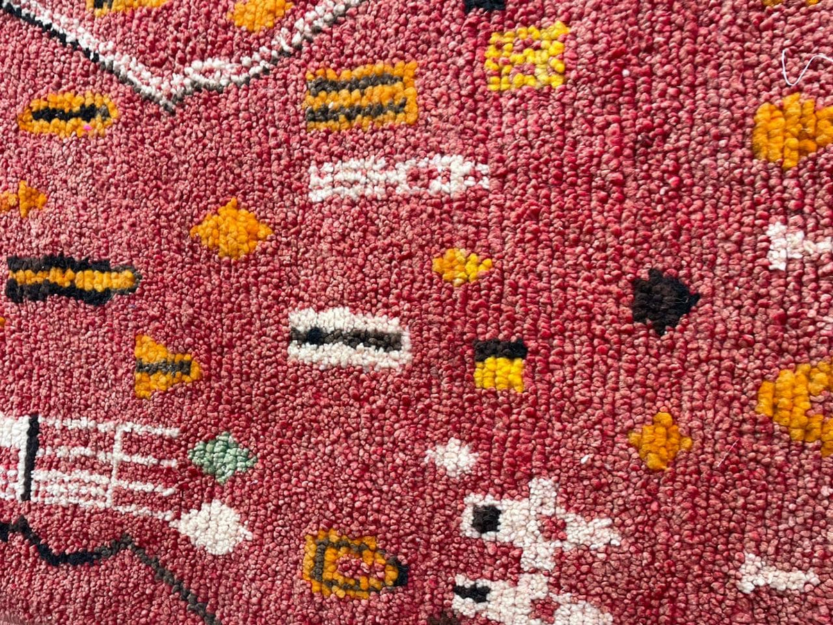 Close-up detail of a vintage Moroccan rug showcasing tribal patterns in green, orange, pink, and cream.