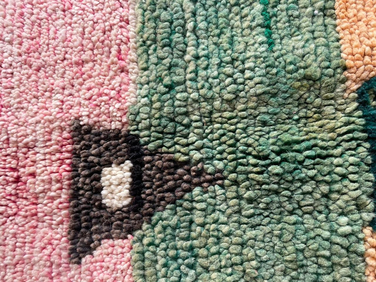 Close-up detail of a vintage Moroccan rug featuring tribal patterns in green, orange, pink, and cream.