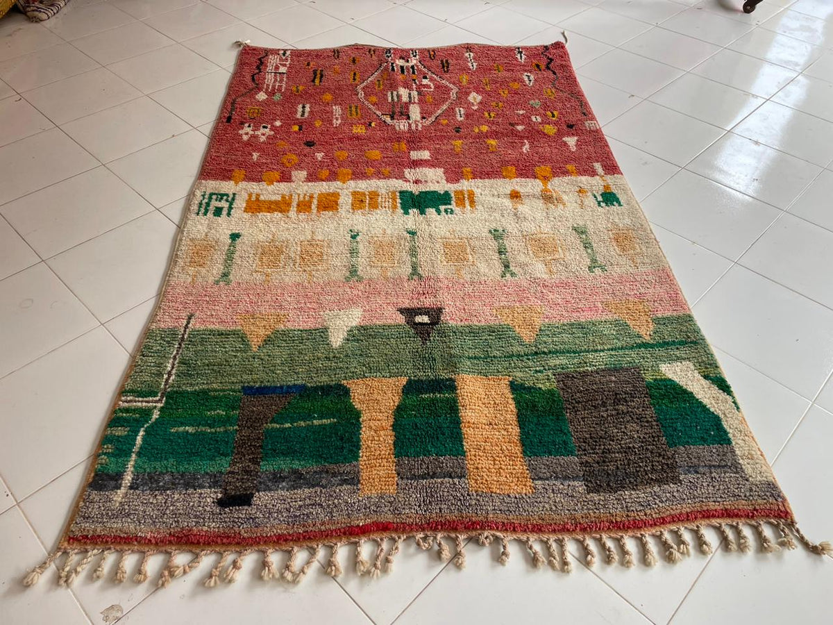 Top view of a vintage Moroccan rug with tribal design and fringed edges in red, green, yellow, and pink.