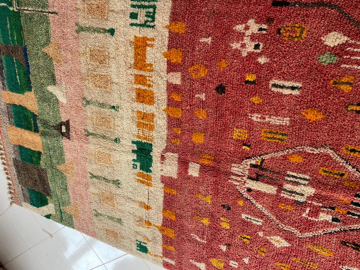 Close-up detail of a vintage Moroccan rug featuring tribal patterns in red, green, orange, and cream.