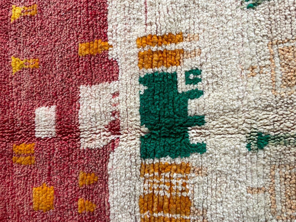 Close-up detail of a vintage Moroccan rug with abstract motifs in red, green, white, and orange.