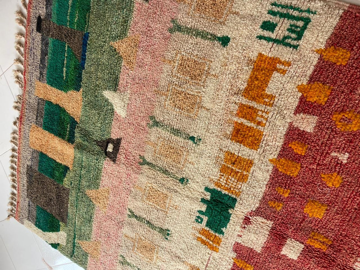 Close-up detail of a vintage Moroccan rug displaying tribal patterns in green, orange, pink, and cream.
