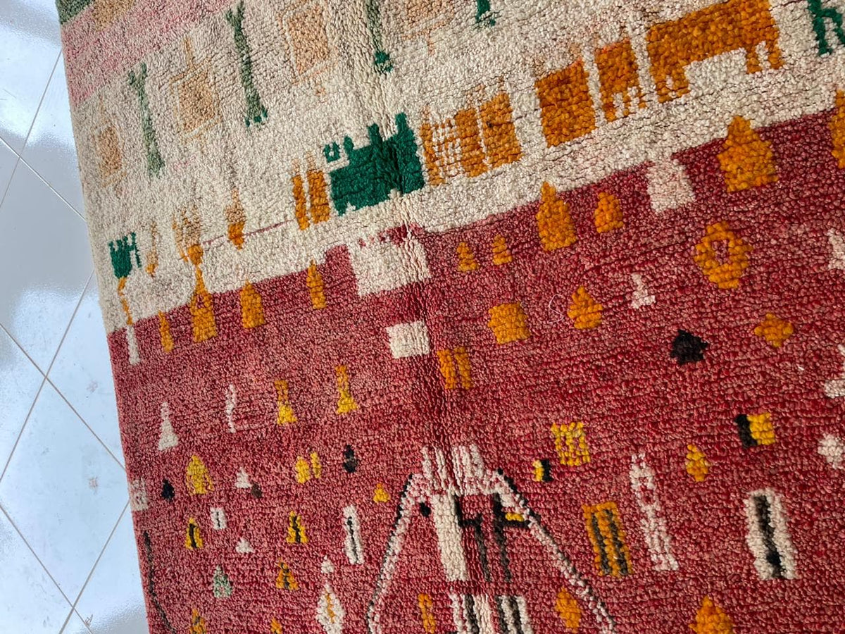 Close-up detail of a vintage Moroccan rug showcasing tribal patterns in red, green, orange, and cream.