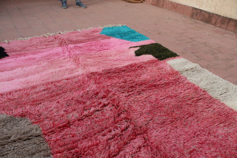 Detail view of a pink Moroccan rug featuring colorful patterns and a textured surface.