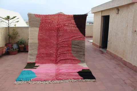 Lifestyle view of a large pink geometric Moroccan rug featuring a textured surface.