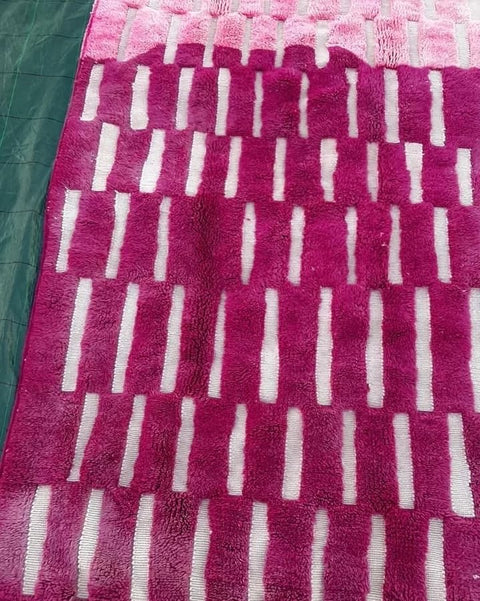 Close-up of a pink Moroccan rug displaying a striped pattern and fluffy texture.