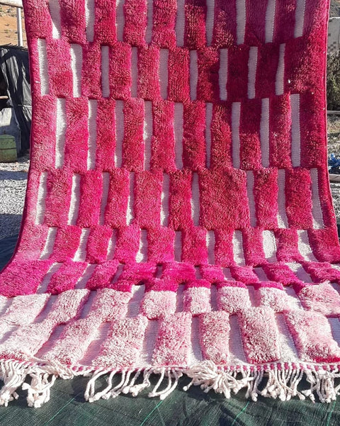 Lifestyle shot of a pink Moroccan rug with geometric pattern and fringe edges.