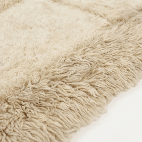 Close-up detail of the edge of the cream and taupe handwoven Beni Ourain rug with fringe.