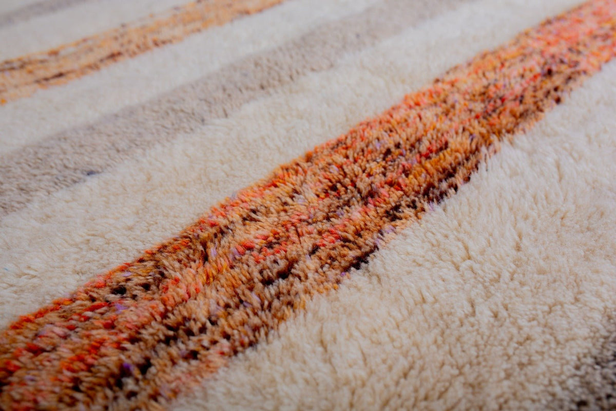 Detailed shot of a Moroccan rug with a striped pattern in white, orange, and brown, featuring a soft texture.