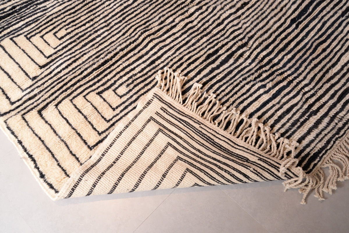 Detail close-up of the corner of the black and beige Moroccan Mrirt rug showing fringe detail.