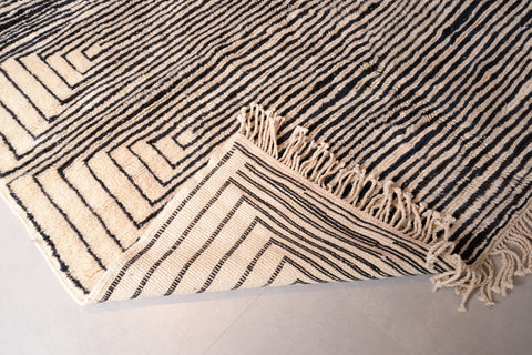 Detail close-up of the corner of the black and beige Moroccan Mrirt rug showing fringe detail.