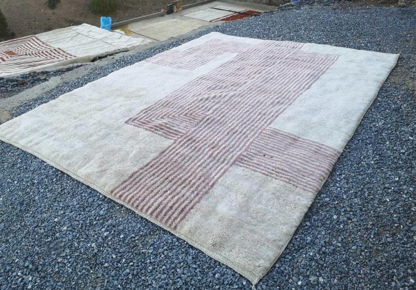 Lifestyle shot of a large Moroccan rug showcasing pink and white abstract patterns in a natural environment.