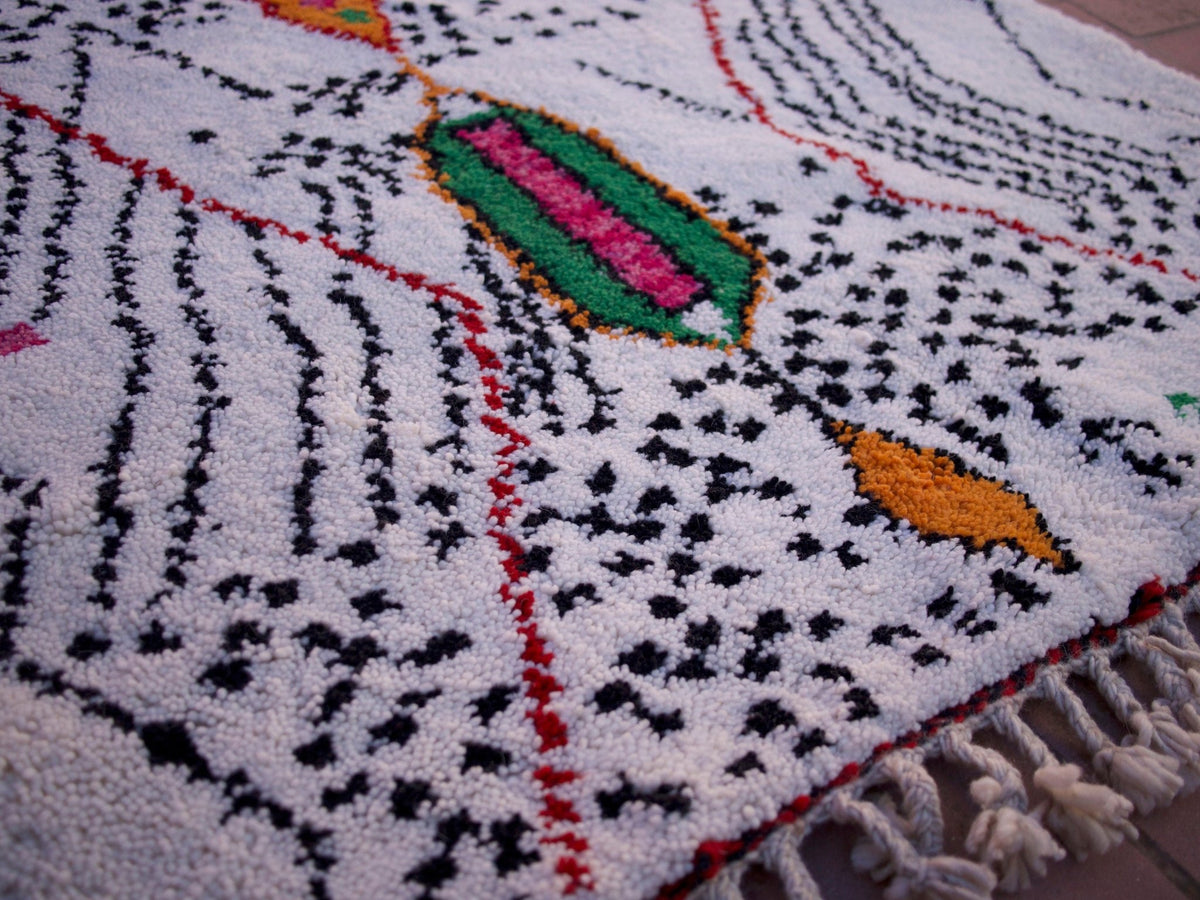Detail view of a multicolor Moroccan rug with geometric designs and fringe edges.