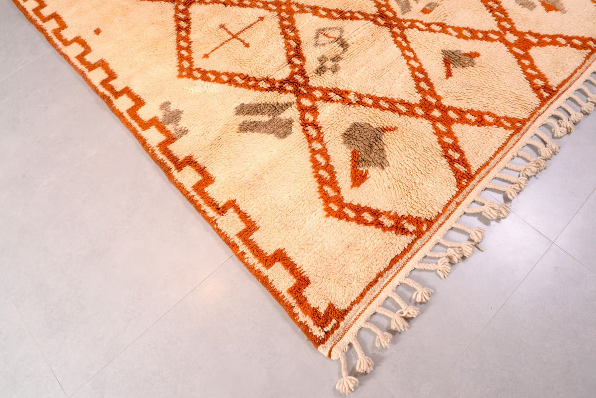 Detailed view of the geometric pattern on the orange Moroccan rug with fringe detail.