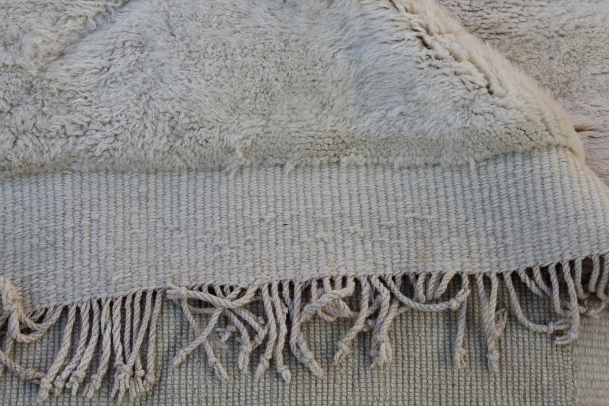 Close-up detail of off-white rug showcasing tufted texture and fringe edges.