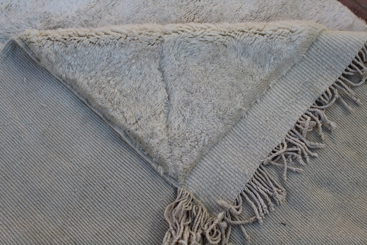 Close-up detail of off-white rug with tufted texture and fringe edges.