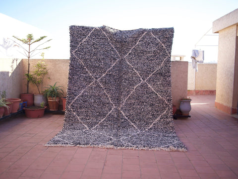 Lifestyle shot of a black Moroccan Beni Ourain rug with geometric patterns in a natural setting.
