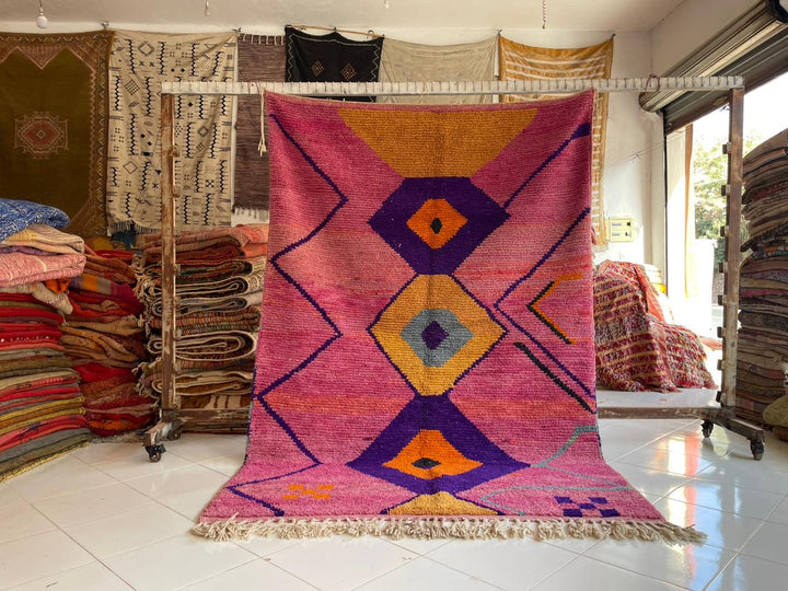 Lifestyle shot of a colorful Moroccan rug featuring geometric patterns and fringe edges.