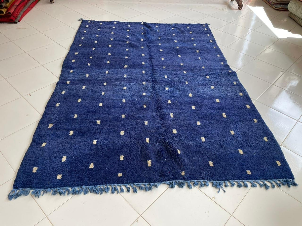 Top view of a blue Moroccan rug featuring fringed edges against a neutral surface.