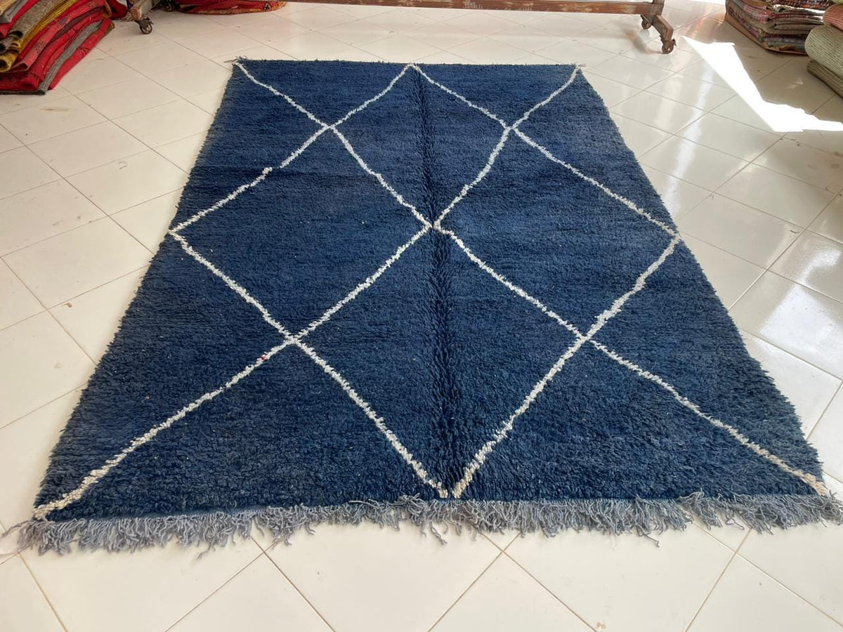 Front view of a blue Moroccan rug featuring fringed edges against a solid color background.