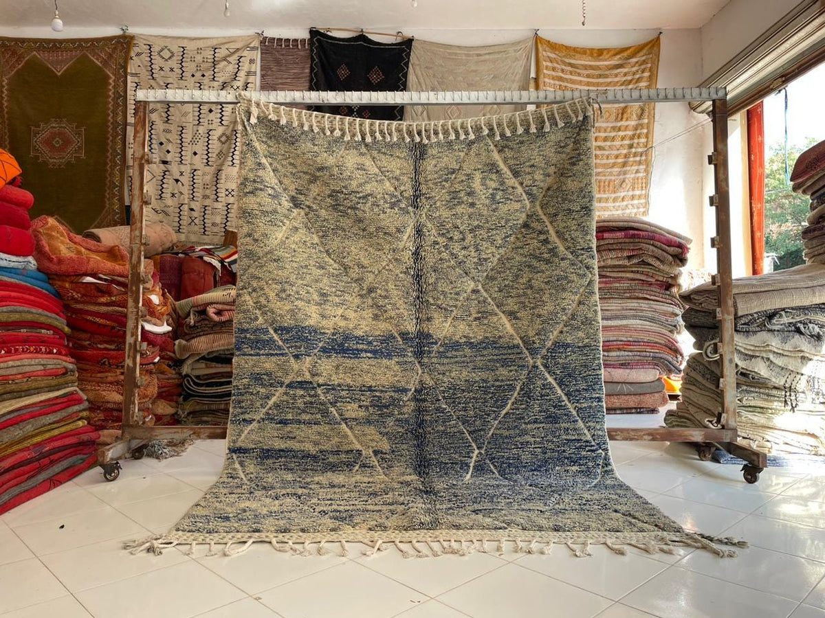 Lifestyle shot of a large blue and black rug with a textured pattern on a natural background.