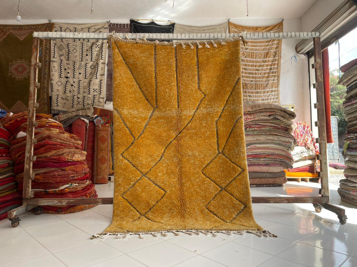 Lifestyle shot of a hanging yellow Moroccan rug with a geometric pattern in a studio setting.