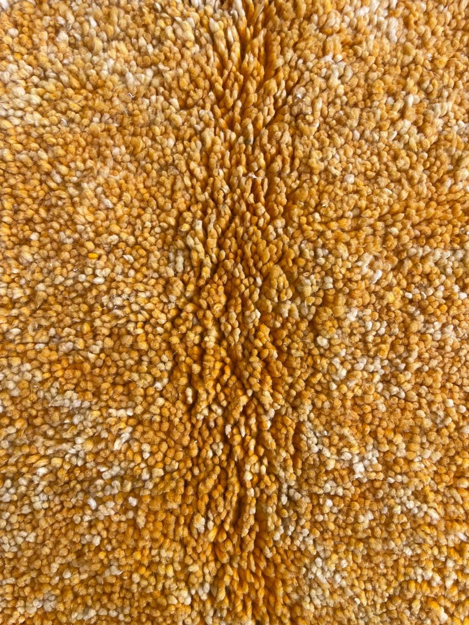 Detail close-up of a yellow textured rug with a soft texture and fringe edges.