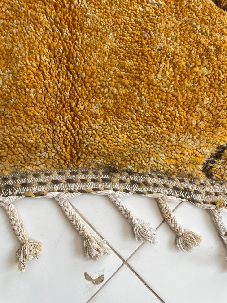 Detail close-up of the edge of a yellow rug showing fringe detail and woven texture.