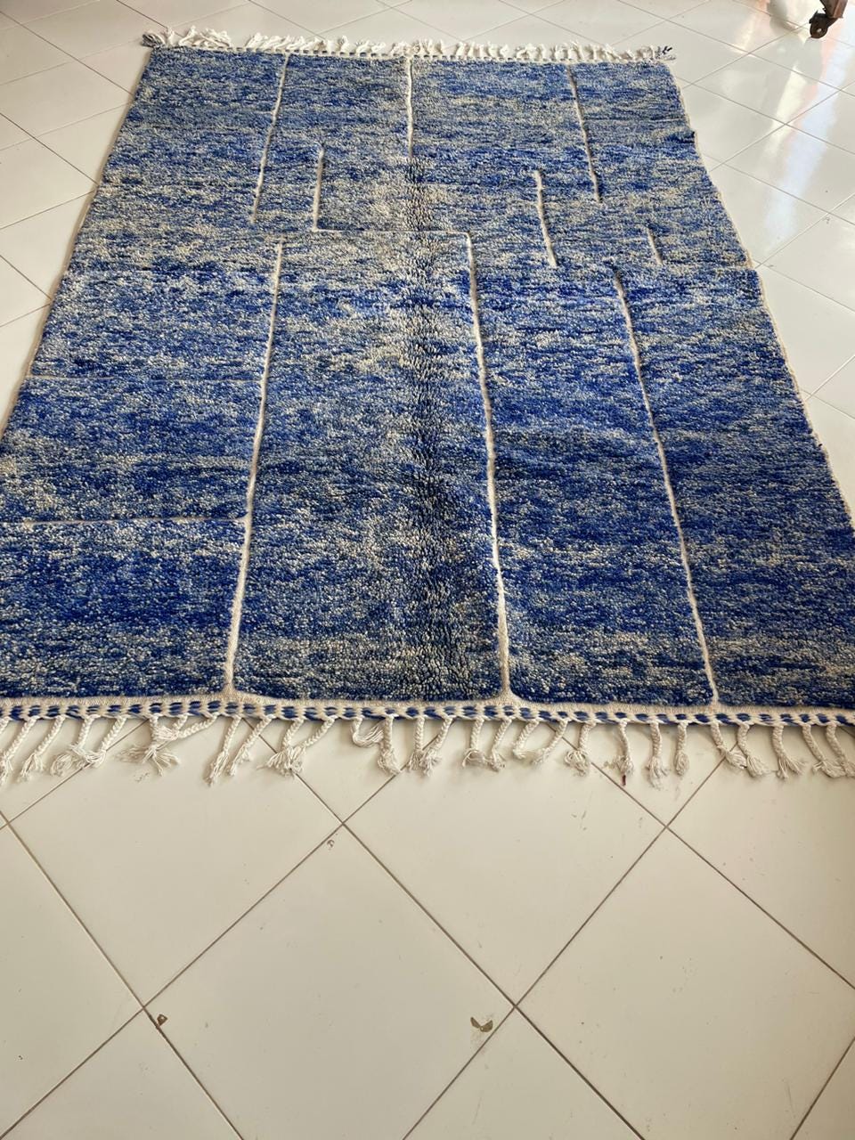 Lifestyle shot of the blue rug featuring geometric patterns and fringed edges.