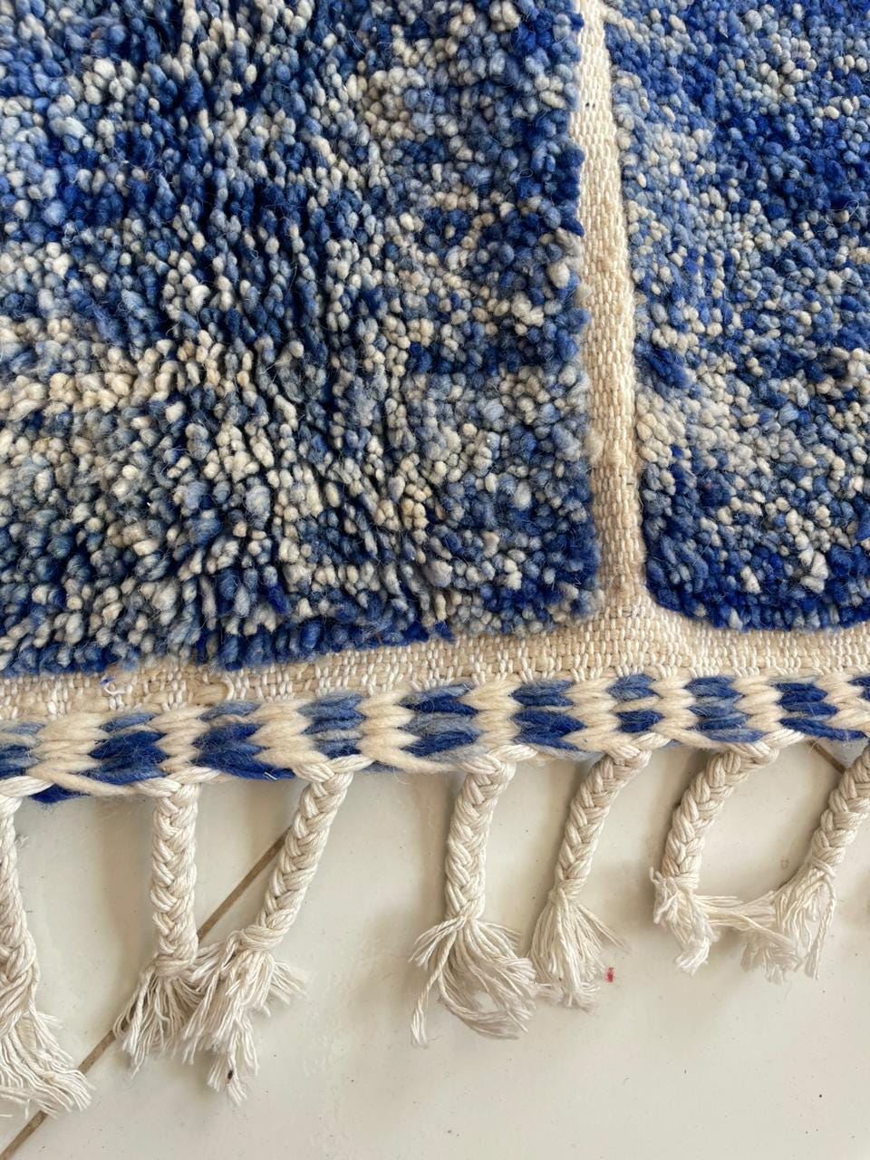 Detail close-up of the blue and beige rug with fringe edges on a white background.