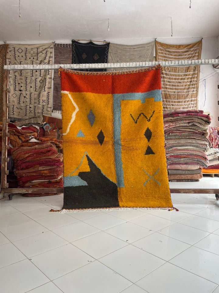 Lifestyle shot of a colorful Moroccan rug with geometric patterns in orange, black, blue, and red.