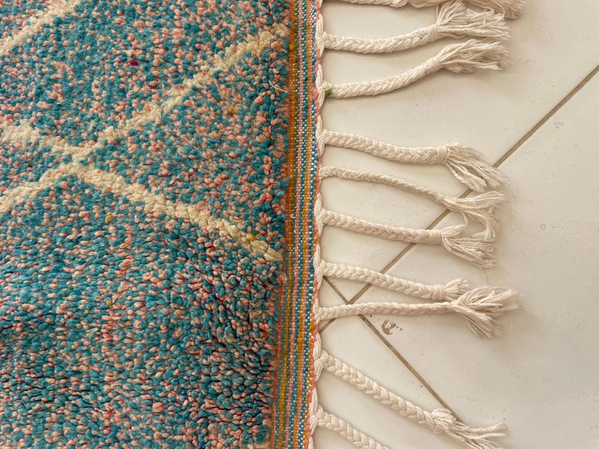Detail shot of a colorful Moroccan rug with fringe edges and a geometric pattern in black and orange.