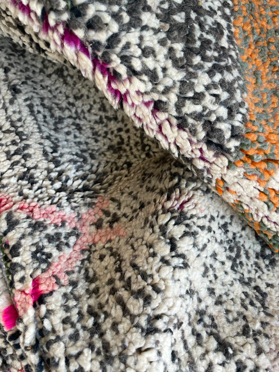 Close-up of a colorful Moroccan rug displaying handmade geometric patterns in black, white, orange, and pink.