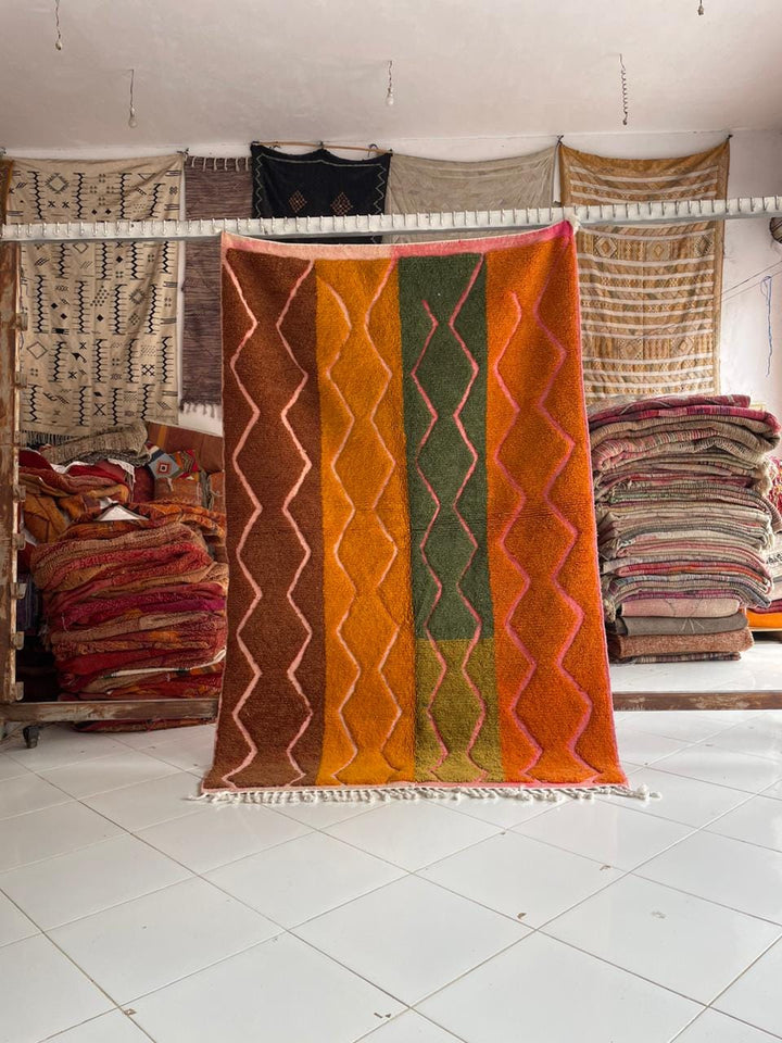 Lifestyle shot of a colorful Moroccan rug with orange, green, and brown tones in a natural setting.