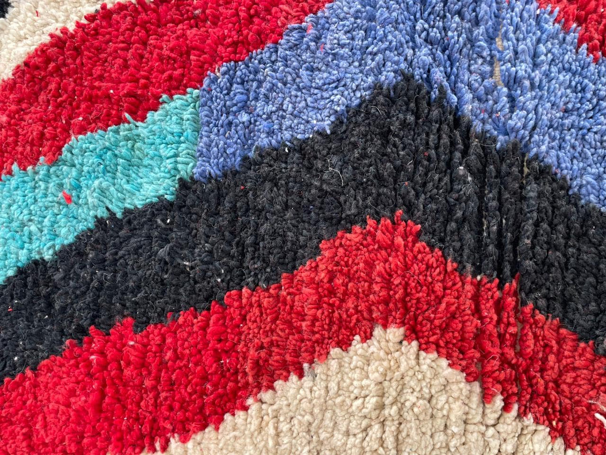 Top view of a colorful Moroccan rug showcasing a chevron pattern in red, blue, orange, and cream.