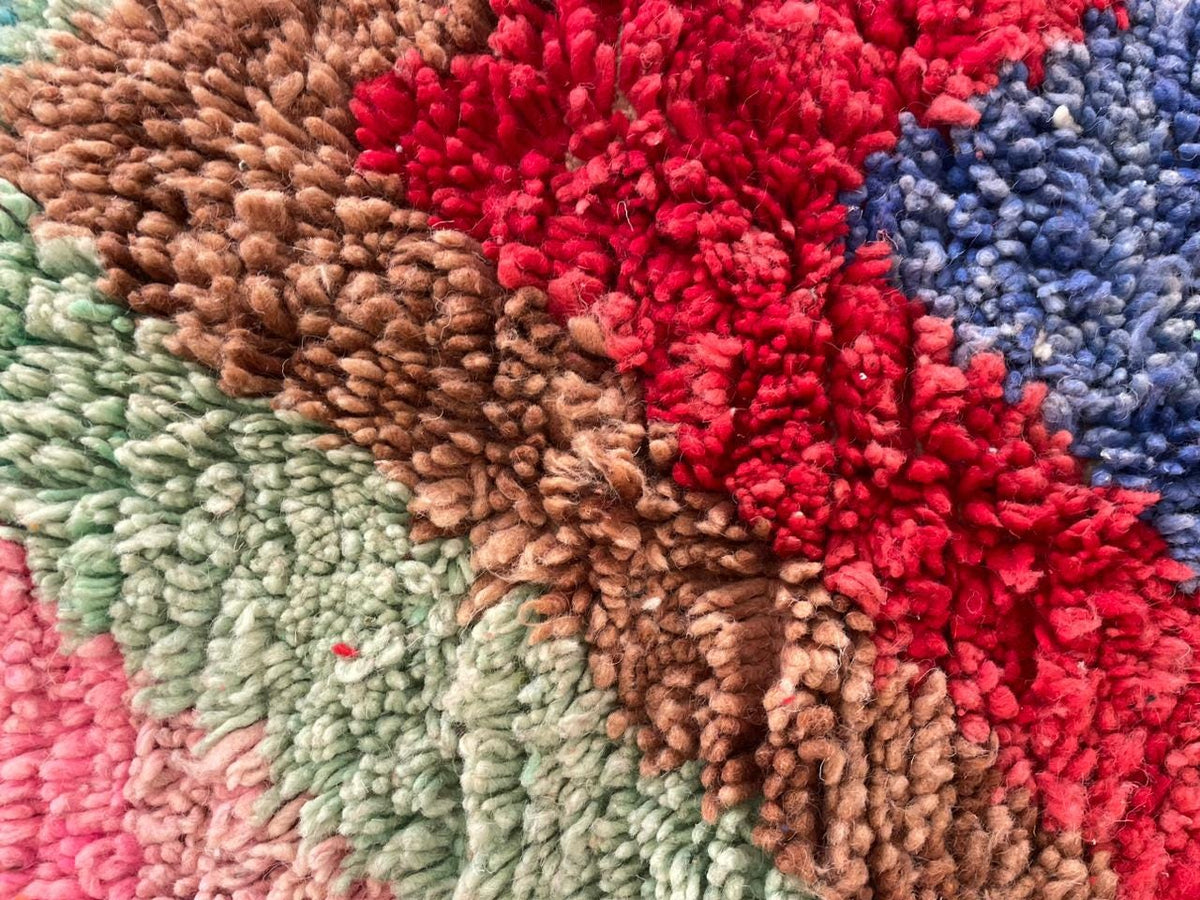 Close-up of a colorful rug featuring a handmade design with red, green, brown, and blue tones.
