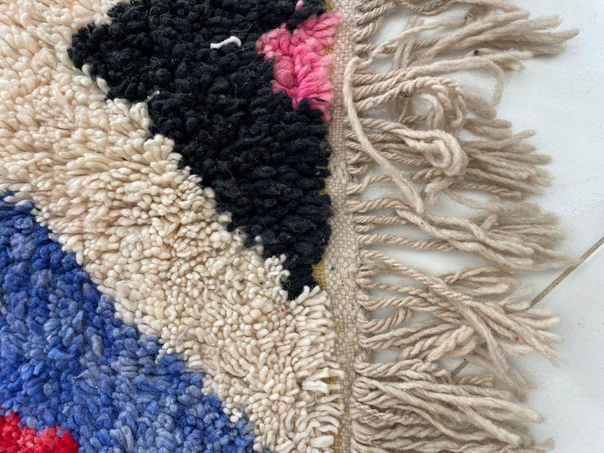Close-up of a colorful rug featuring fringe detail and a textured surface in beige, black, and pink.
