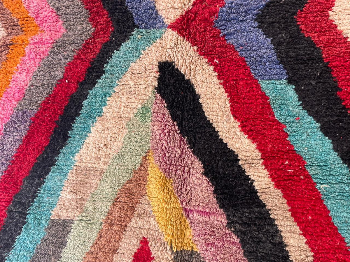 Detail shot of a colorful rug with a zigzag pattern in red, black, pink, and turquoise.