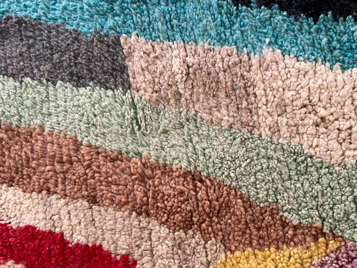 Close-up of a colorful rug displaying geometric patterns in red, pink, black, and yellow.