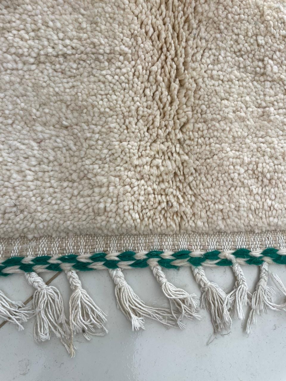 Detail close-up of a handmade rug featuring fringe detail and a textured surface.