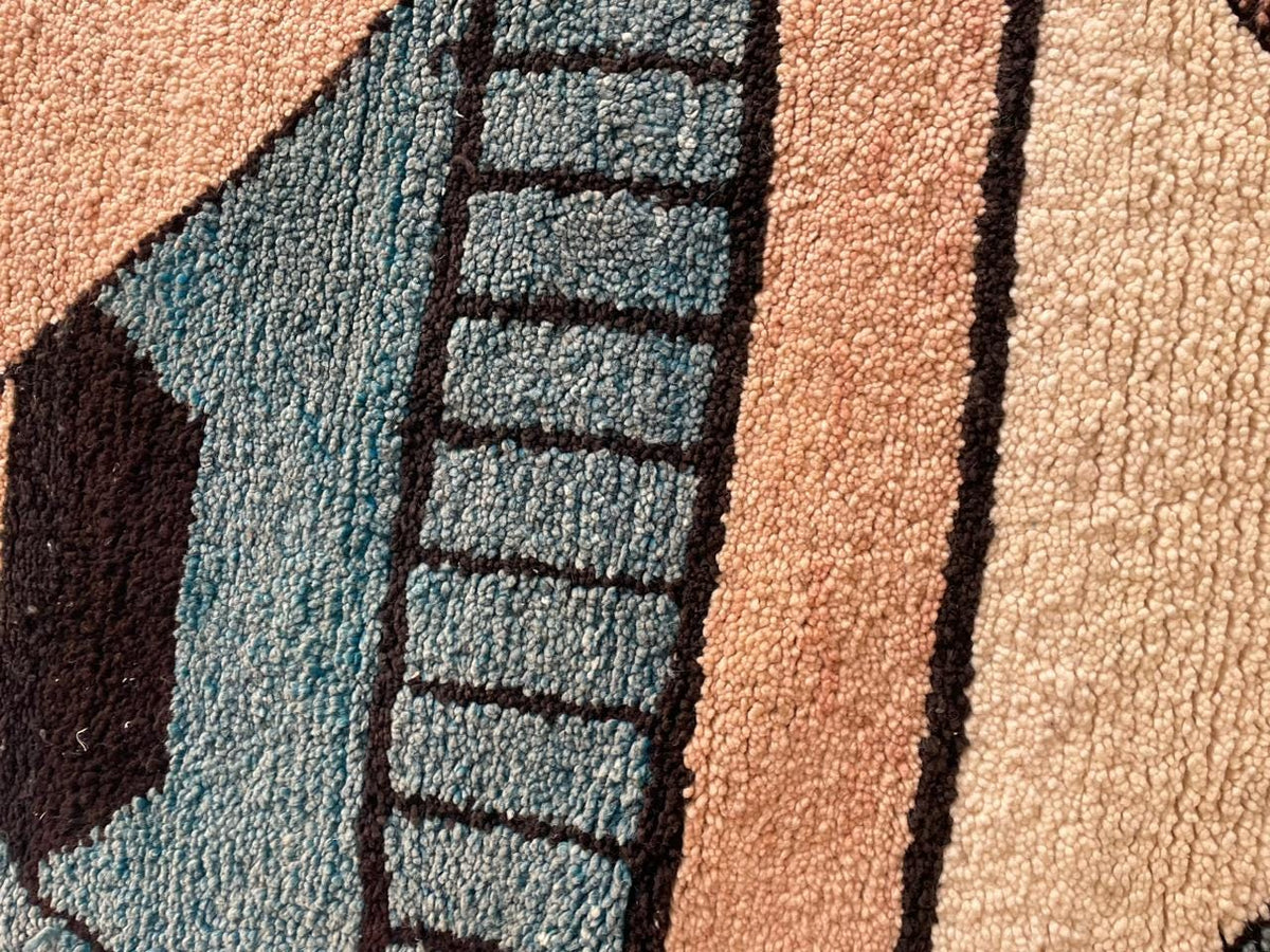 Close-up detail of a Moroccan rug featuring an abstract design with a thick pile in blue, beige, and brown.