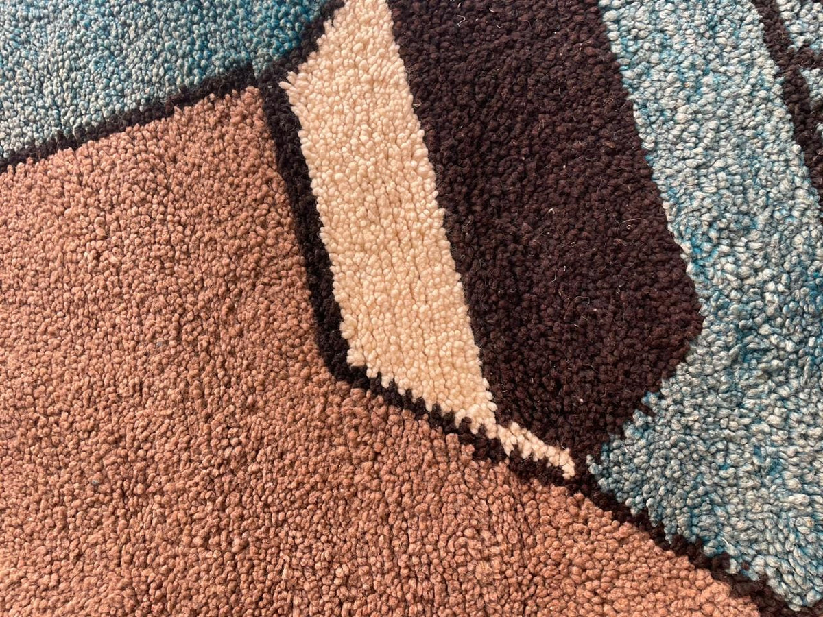 Close-up detail of the textured surface of a colorful Moroccan rug featuring geometric design in blue, brown, and cream.