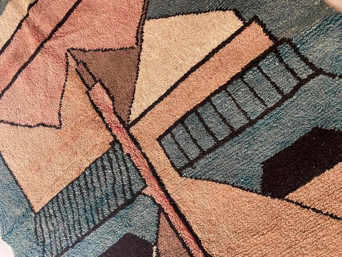 Close-up detail of the textured surface of a colorful Moroccan rug with geometric design in blue, brown, and cream.