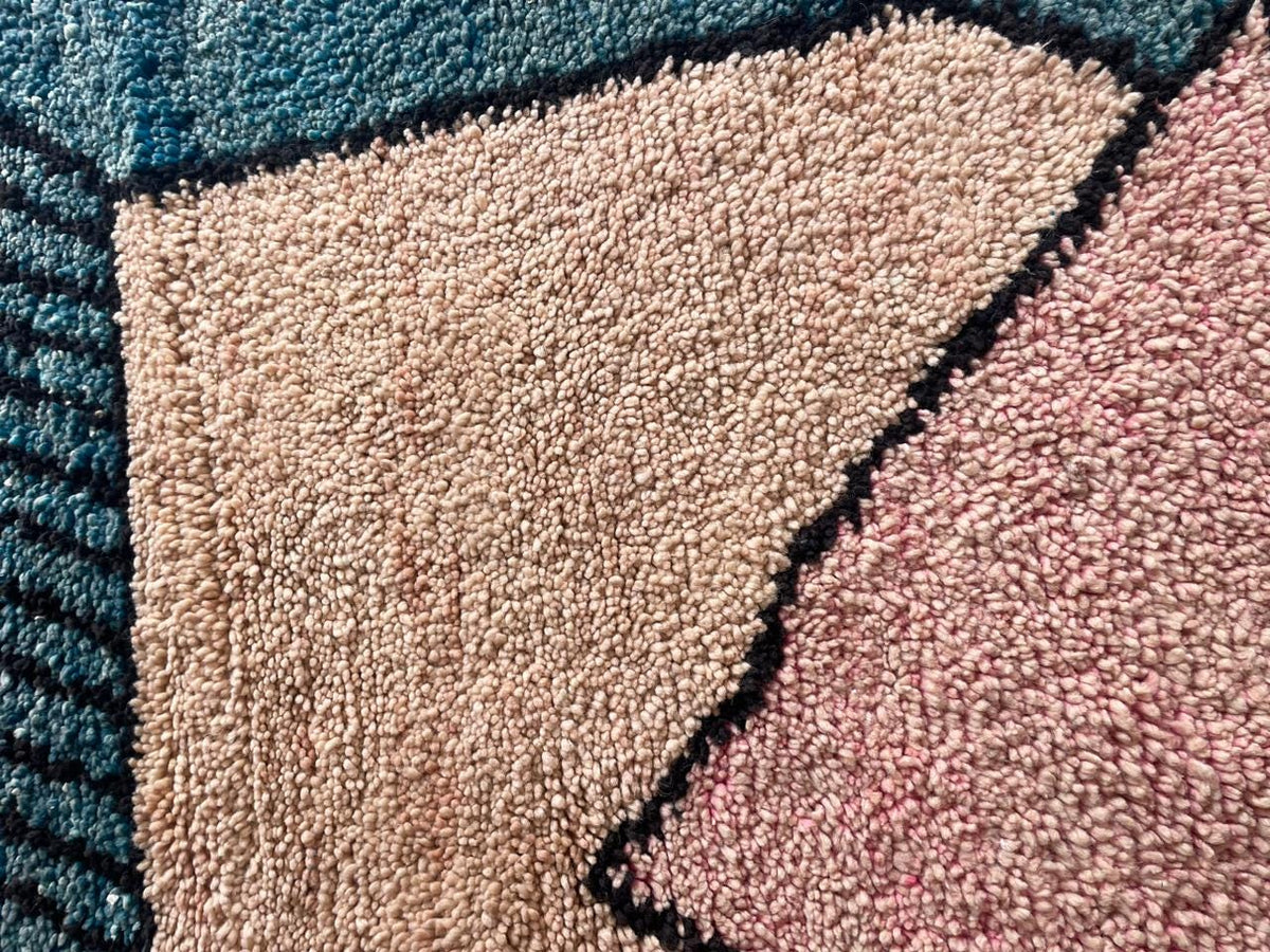 Close-up detail of a Moroccan rug with a geometric pattern in blue, pink, and beige.